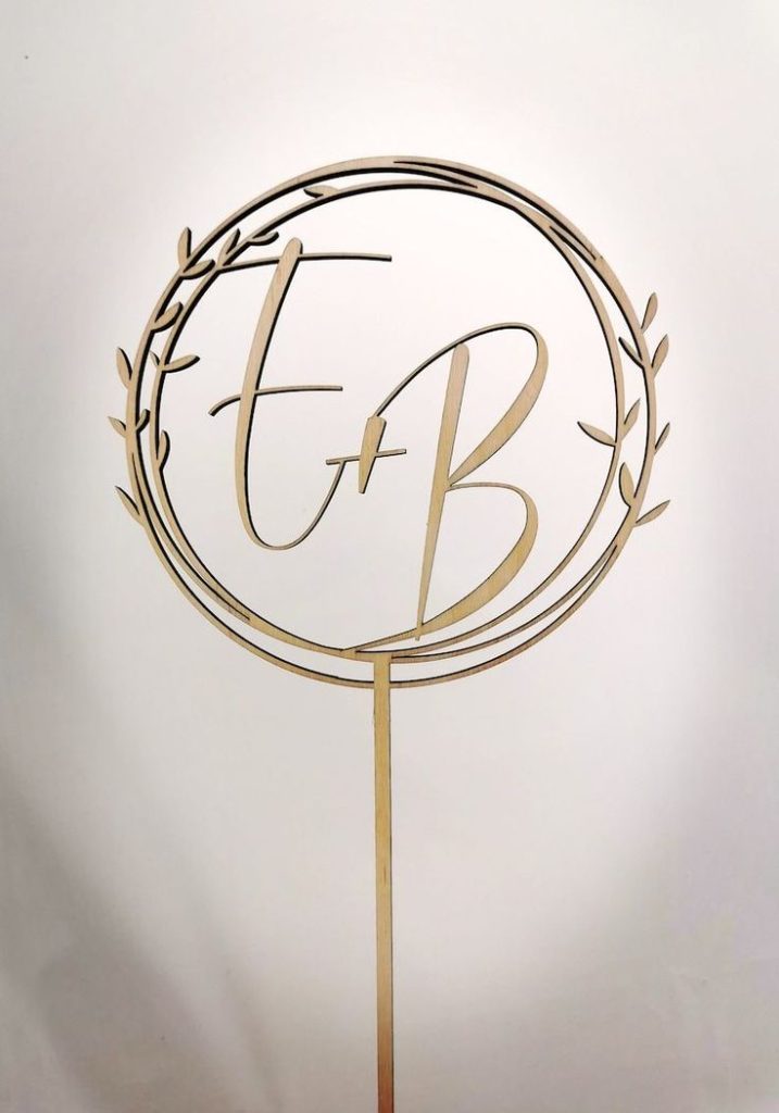 Cake Topper Hochzeit personalisiert: So gestaltest du deine Torte mit eurer Liebesgeschichte Hochzeitsplanung, Hochzeitsblog Ein moderner Cake Topper in Gold mit den verschlungenen Initialen des Paares, eine stilvolle Wahl für einen Hochzeit Cake.