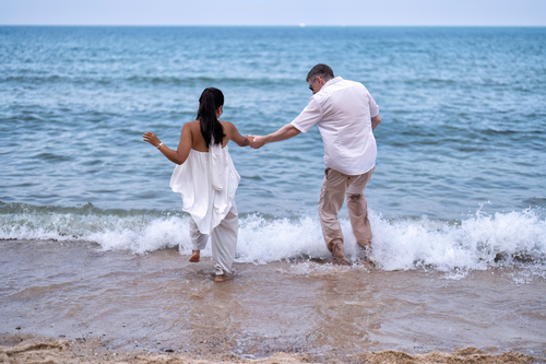 Frisch vermähltes Paar tanzt oder spaziert nach ihrer Strandhochzeit ins Meer.